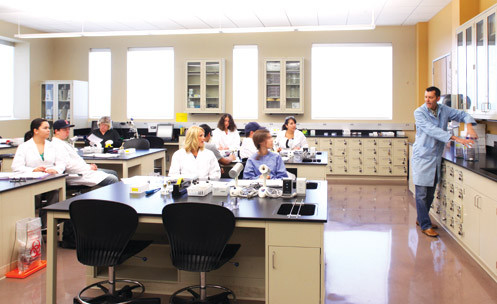 A class of students in lab coats watches an instructor.