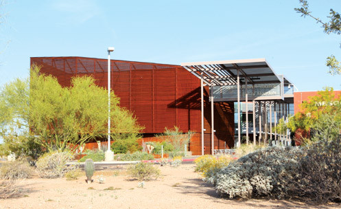 The exterior of a red building with desert landscaping in front.