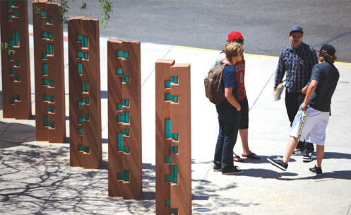 Four students chatting outside near a row of pillars.