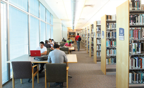 Students studying in the library near stacks of books.