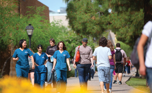 Many students walking on a campus path, some in scrubs.