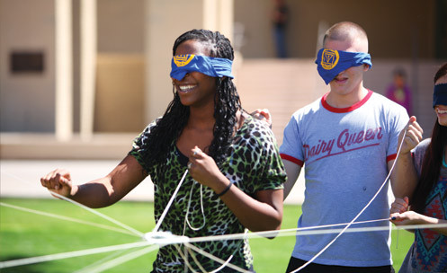 Three students with eyes covered smile and pull on strings as a game.