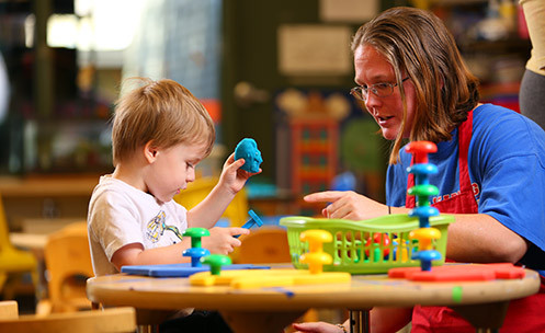 Adult and child sitting at a table playing with blocks in a preschool setting