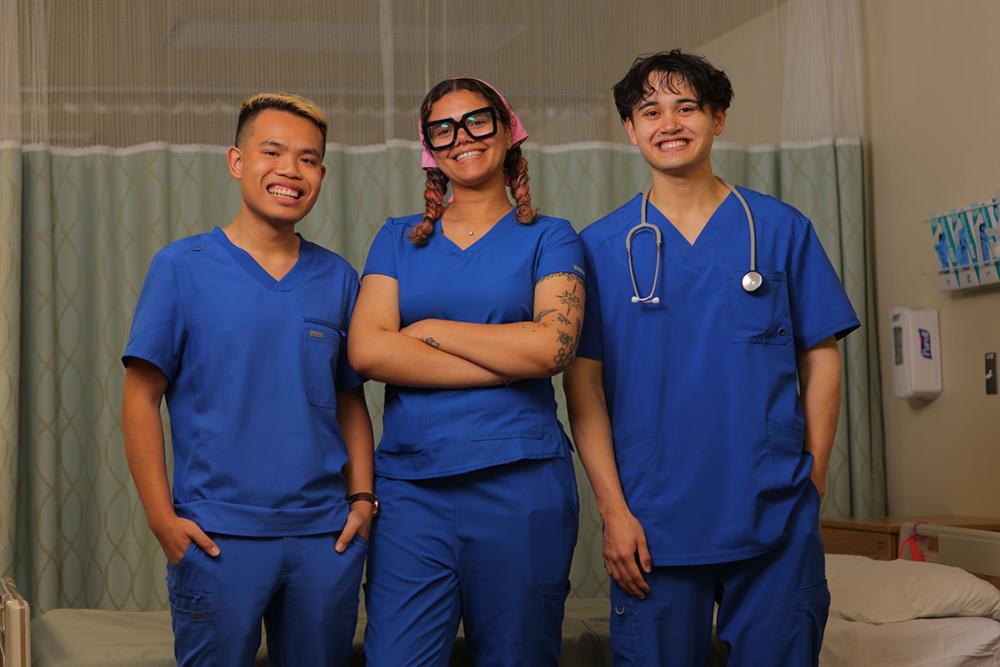 Three students wearing scrubs in a hospital room.