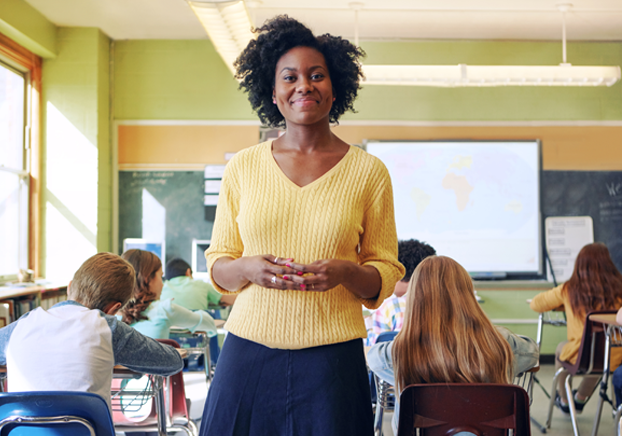 Teacher standing at the back of the classroom smiling.