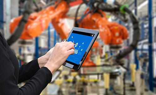 Hands using a tablet with robotic arms in the background.