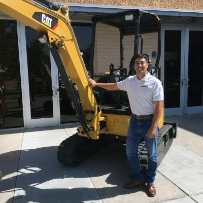 Diego Santos posing in front of a CAT backhoe.