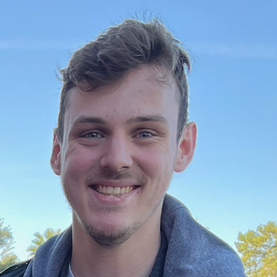 Man smiling wearing white t-shirt and black and gray jacket.
