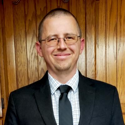 Smiling man with glasses, coat and tie.
