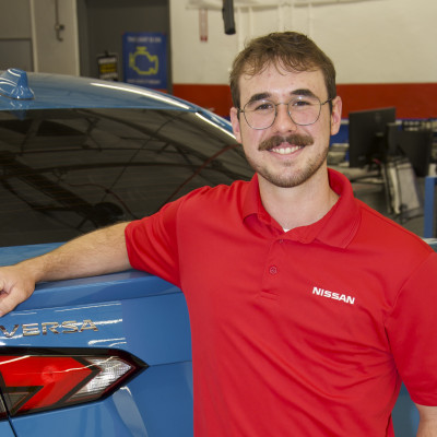 Nathan Schroeder in the MCC Automotive Service lab with his arm propped on the back of a Nissan Versa. 