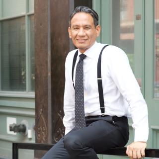 Manuel Romero sitting on a railing in dress clothes.