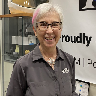 Pam Waterman in a grey shirt, wearing glasses, smiling.