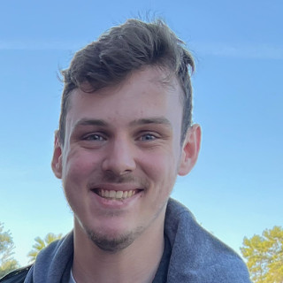 Man smiling wearing white t-shirt and black and gray jacket.
