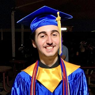 Smiling male teenager in blue graduation cap and gown.