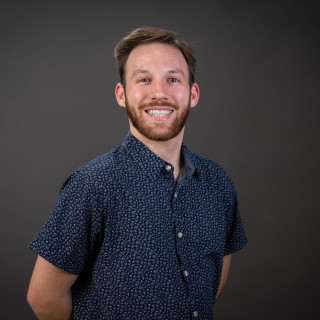 Joseph Katz posing in a dark colored colared shirt. 