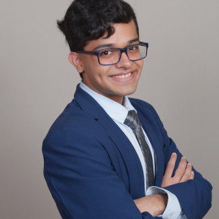 Pranay Modha, a smiling young man with short dark hair wearing dark rimmed glasses and a blue suit with a tie. 